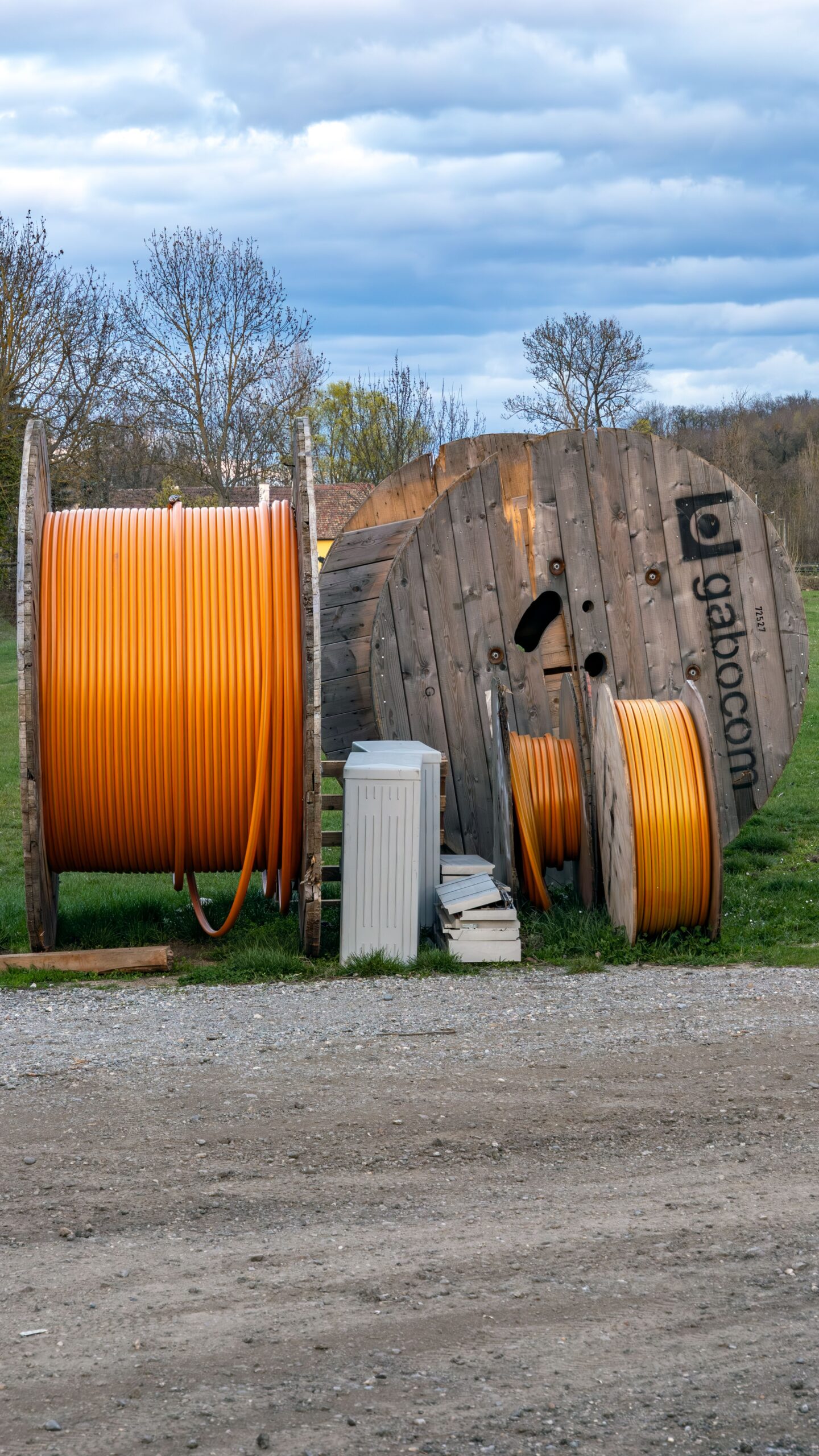 Wooden spools holding orange cables in a rural outdoor area.